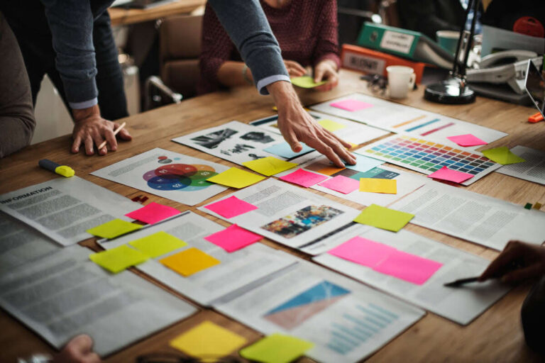 A professional creative team at a branding agency in Noida collaborating on a digital-first brand strategy with mood boards, color palettes, and sticky notes on a wooden desk.