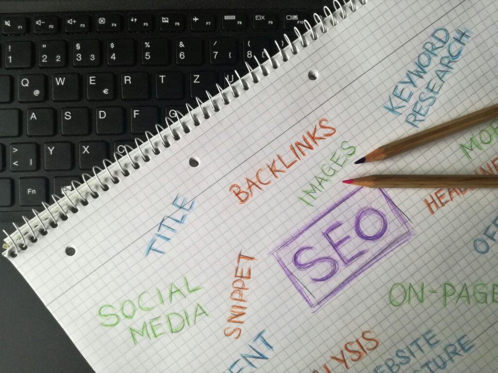 Notebook with handwritten SEO terms like backlinks, keywords, on-page, social media, and content placed beside a keyboard.